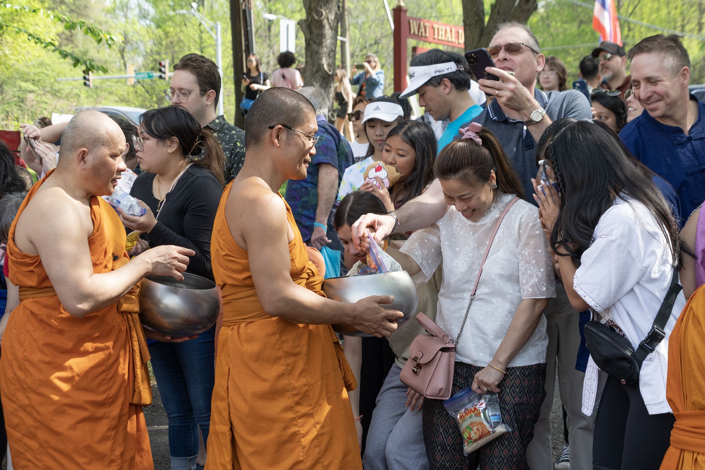 Orange robed monks accept offerings in bowls.