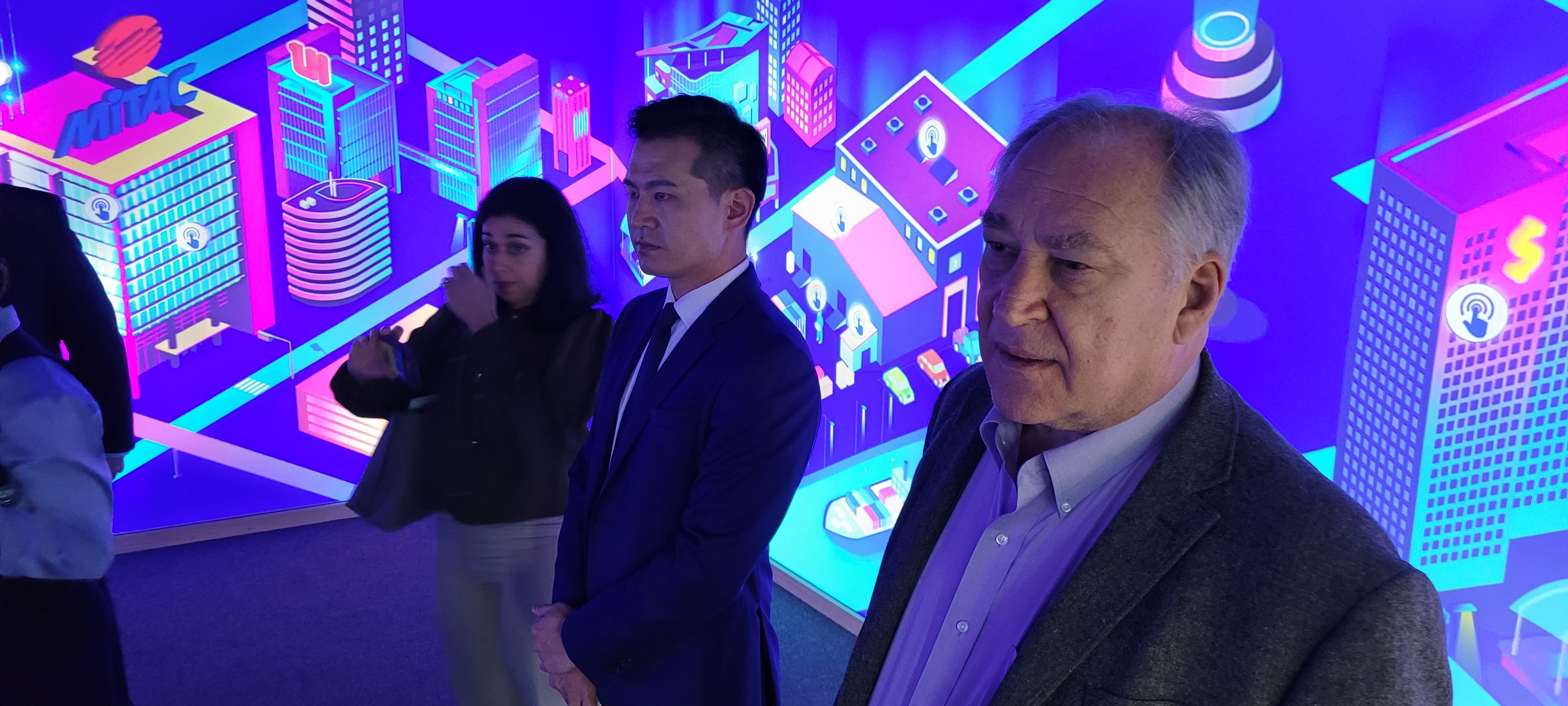 County Executive Marc Elrich speaks with guests, in front of neon background.