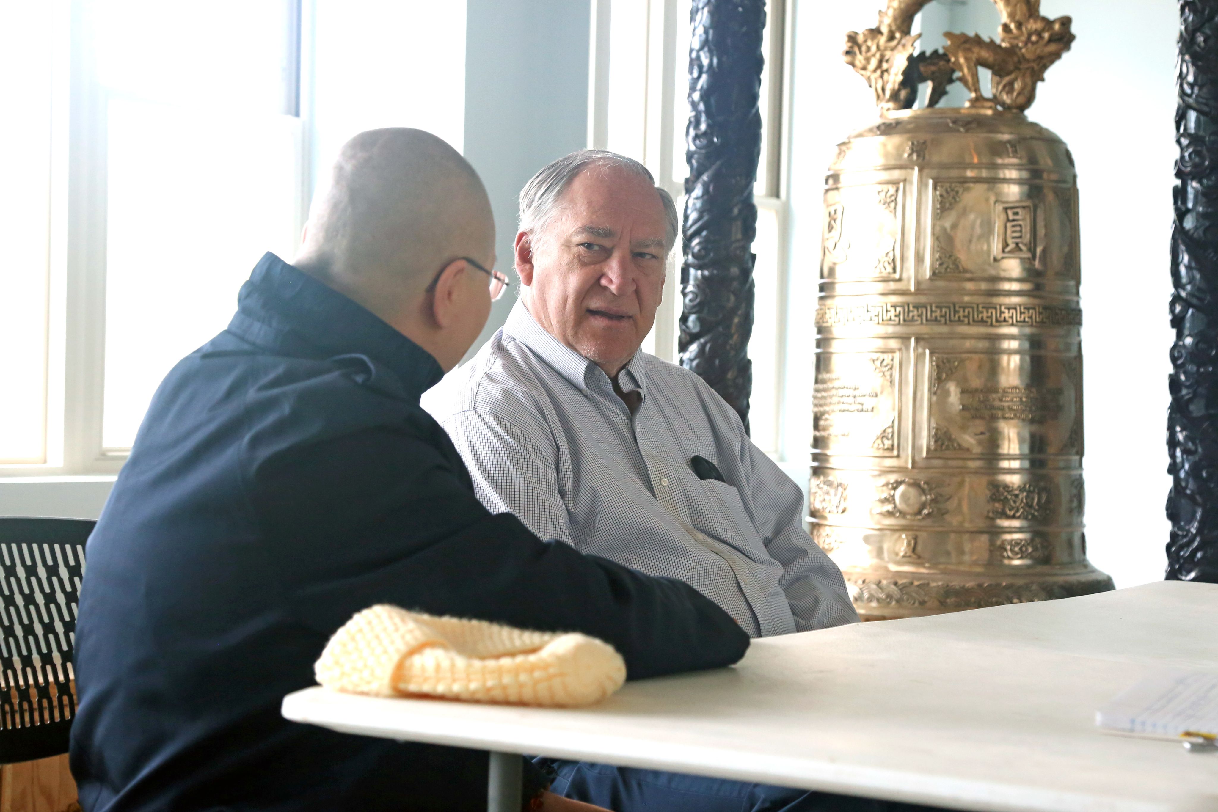 County Executive Marc Elrich speaks with guest, in front of silver temple bell.