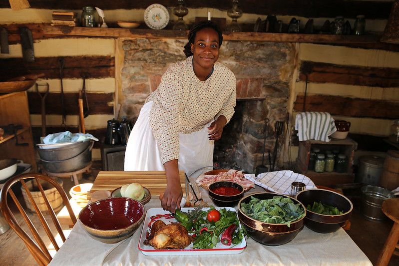 Woman in historic clothing demonstrating plating a meal inside Oakley Cabin